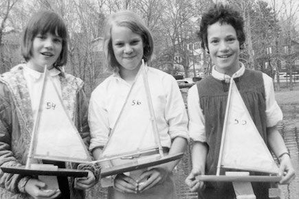 Three students posing with their sailboats and smiling.