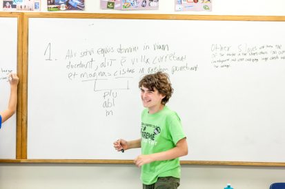 A student smiling while working at a whiteboard in class.