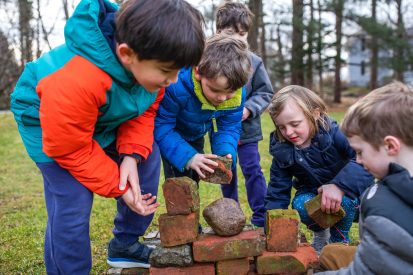 Students working on putting together a brick wall outside.