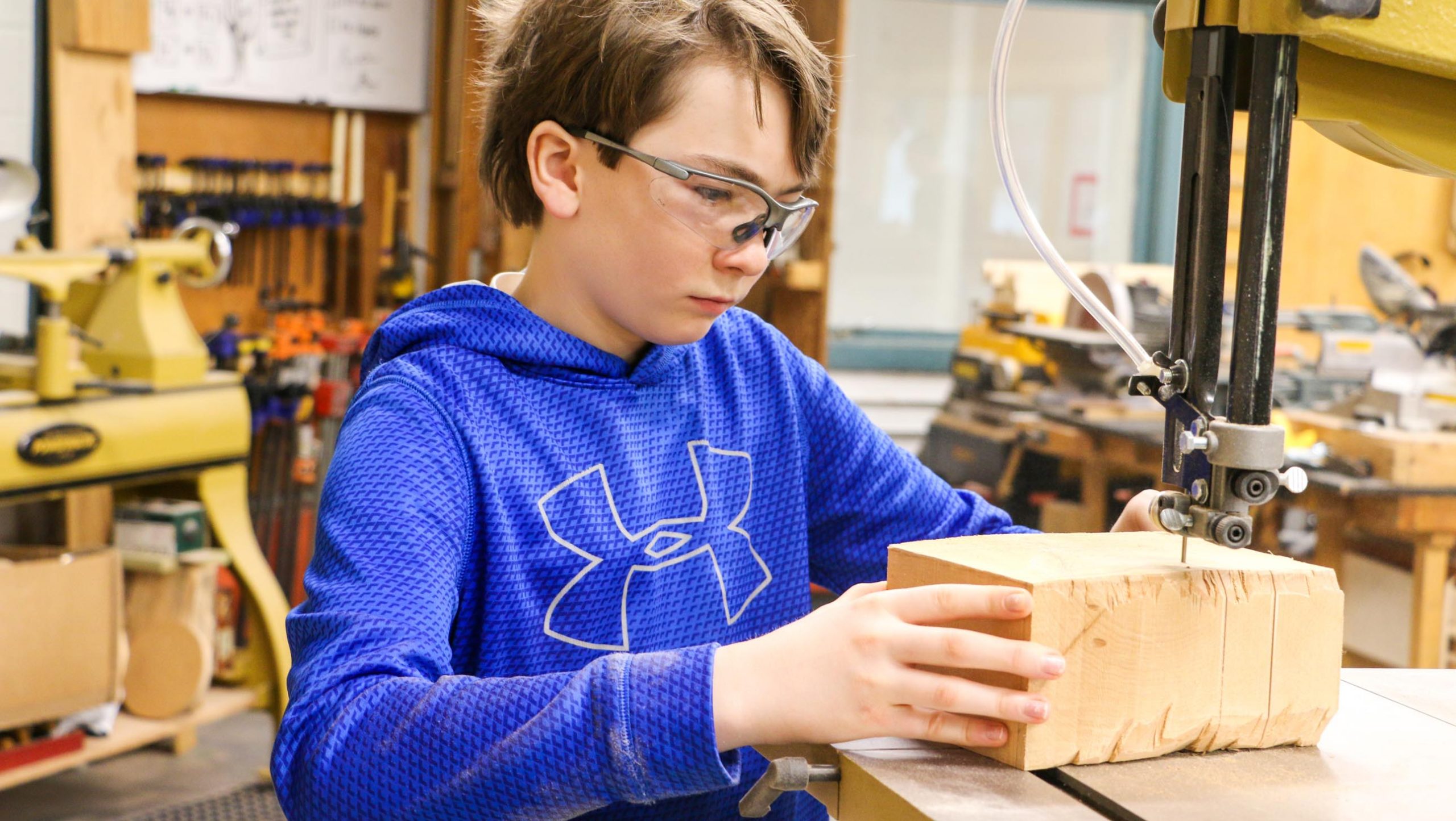 A student cutting a piece of wood using a band saw.