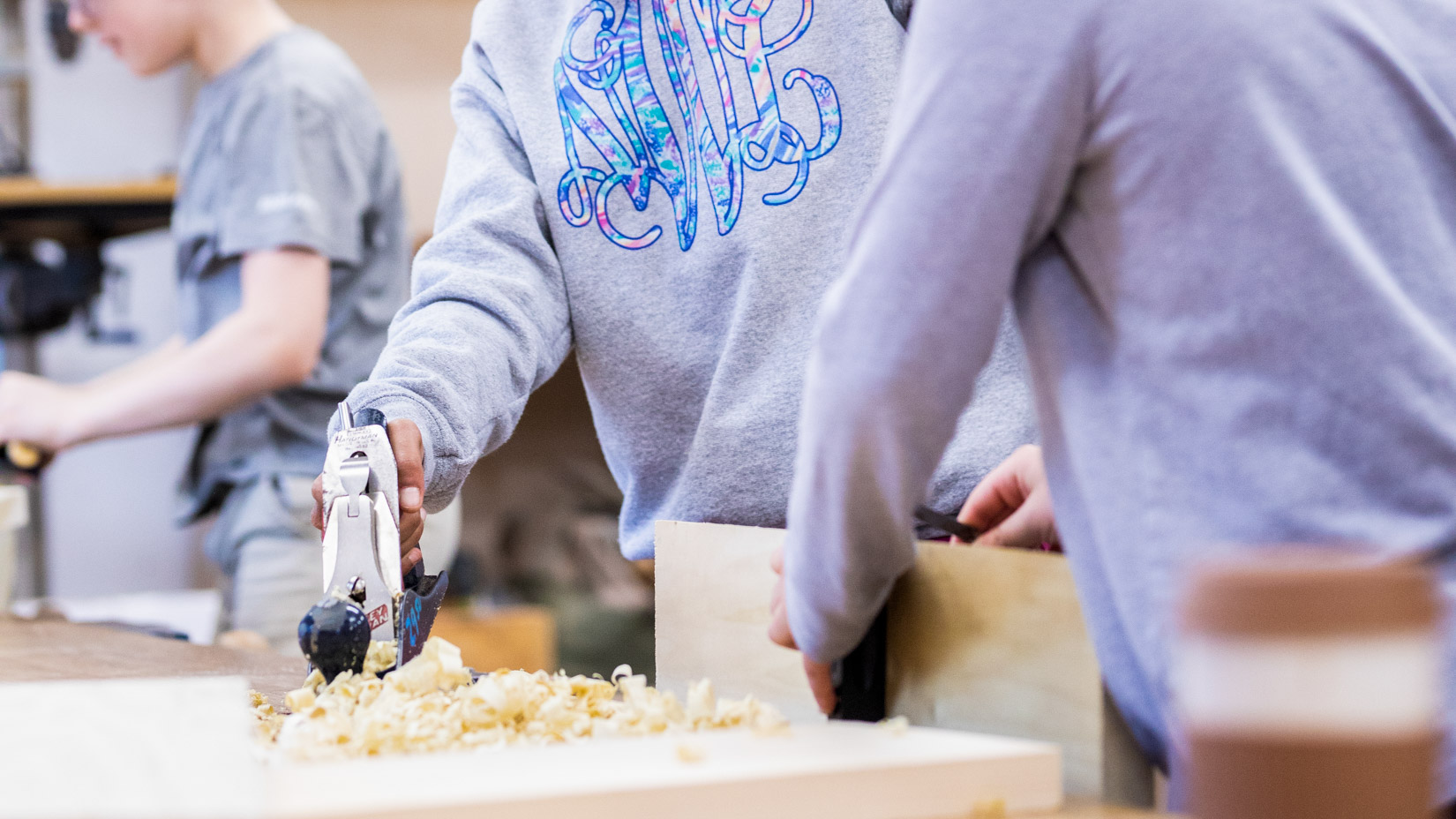 Two students using a planer on a plank of wood.