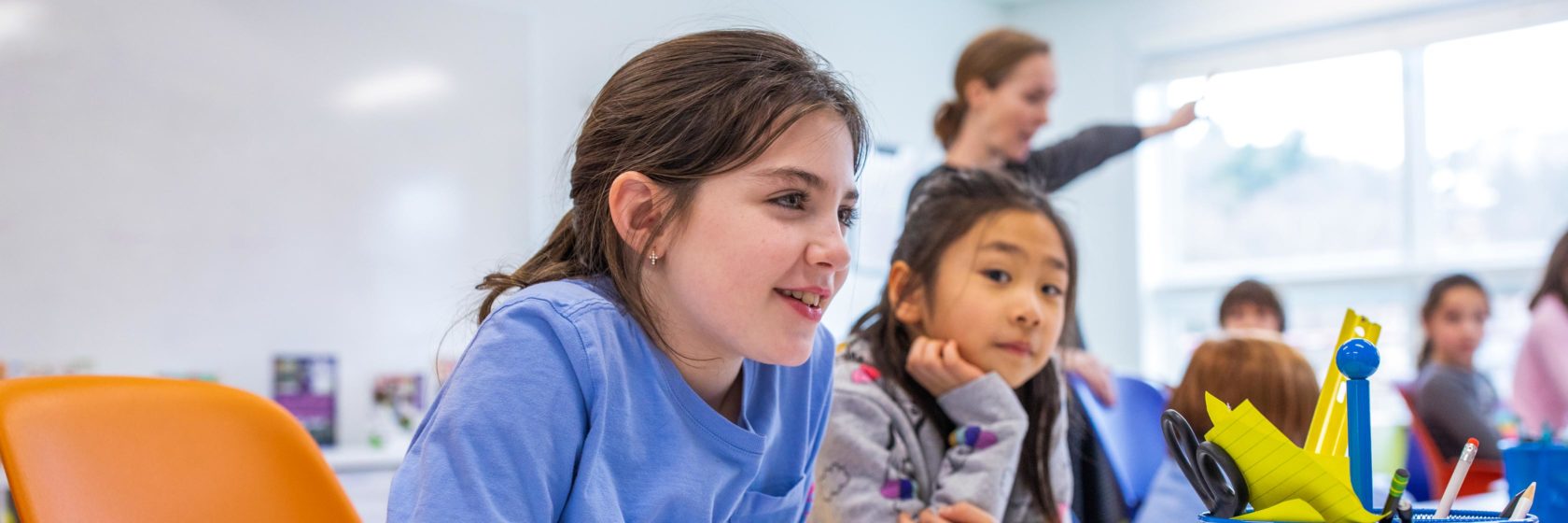 A student smiling while in class and listening to the teacher