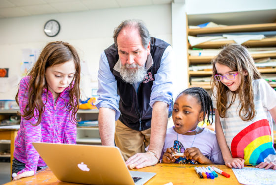 A teacher showing three students something on the computer.