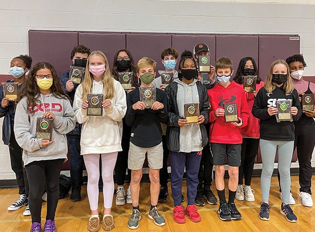 Students standing in the gym holding sports awards