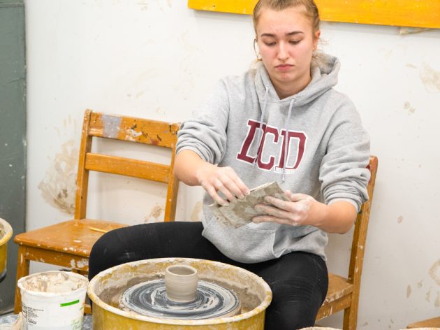 A student using a pottery wheel to make a clay creation.