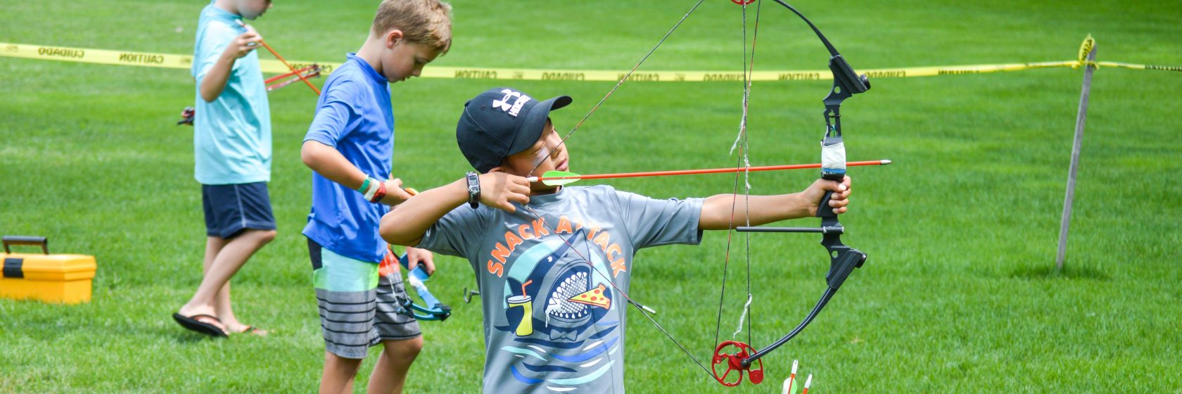 A camper shooting a bow and arrow aiming to hit a target in the distance.