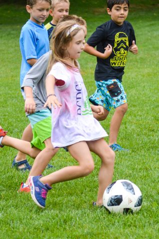 A girl playing soccer with other campers.