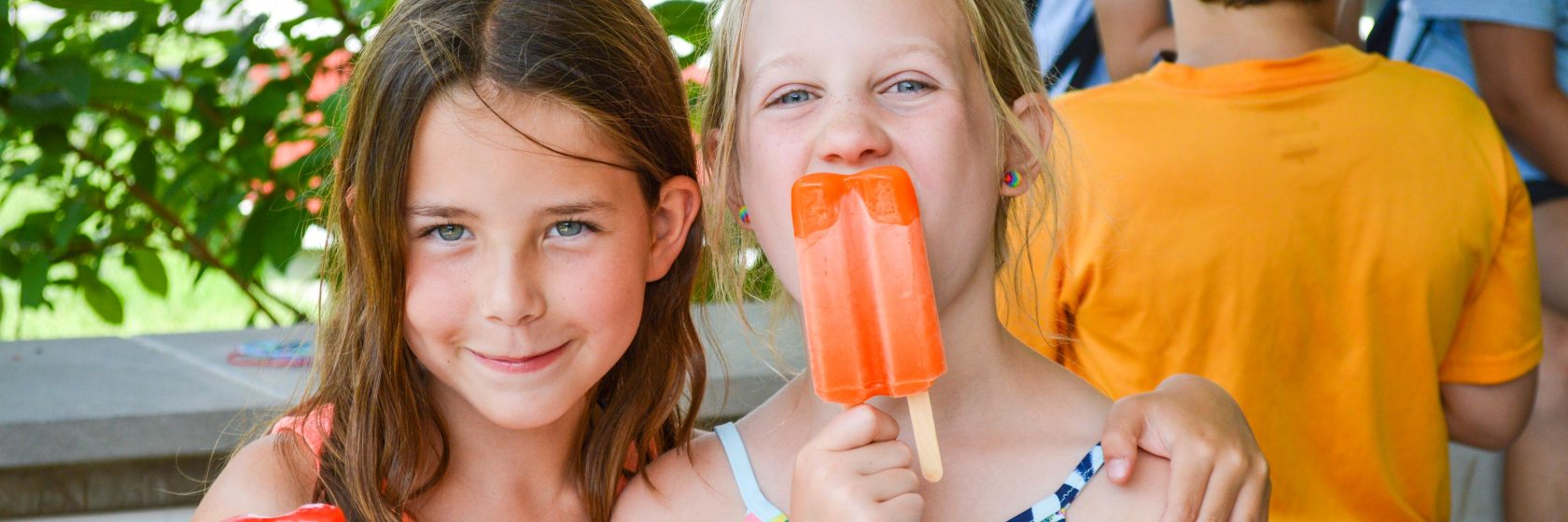 Two girls at camp having ice cream popsicles.