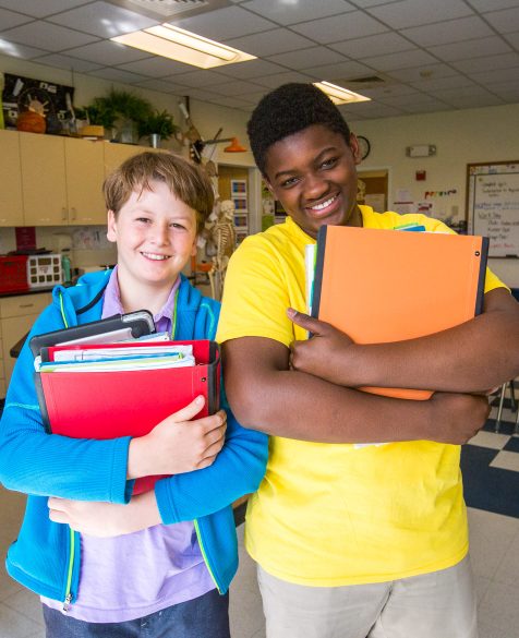Two students standing with their books and smiling in a classroom.