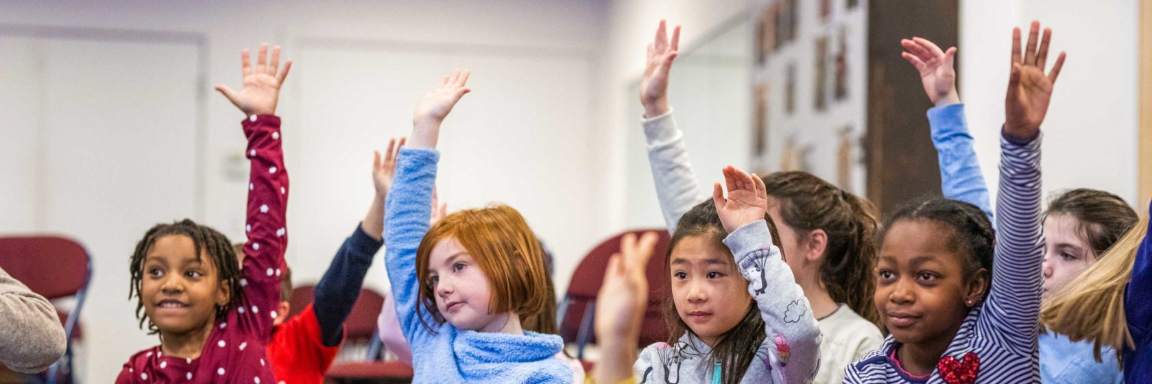 Children raising their hands to ask questions while in class.