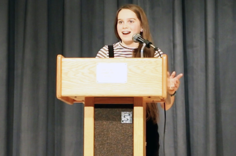 An eighth grader standing at a podium getting ready to speak.