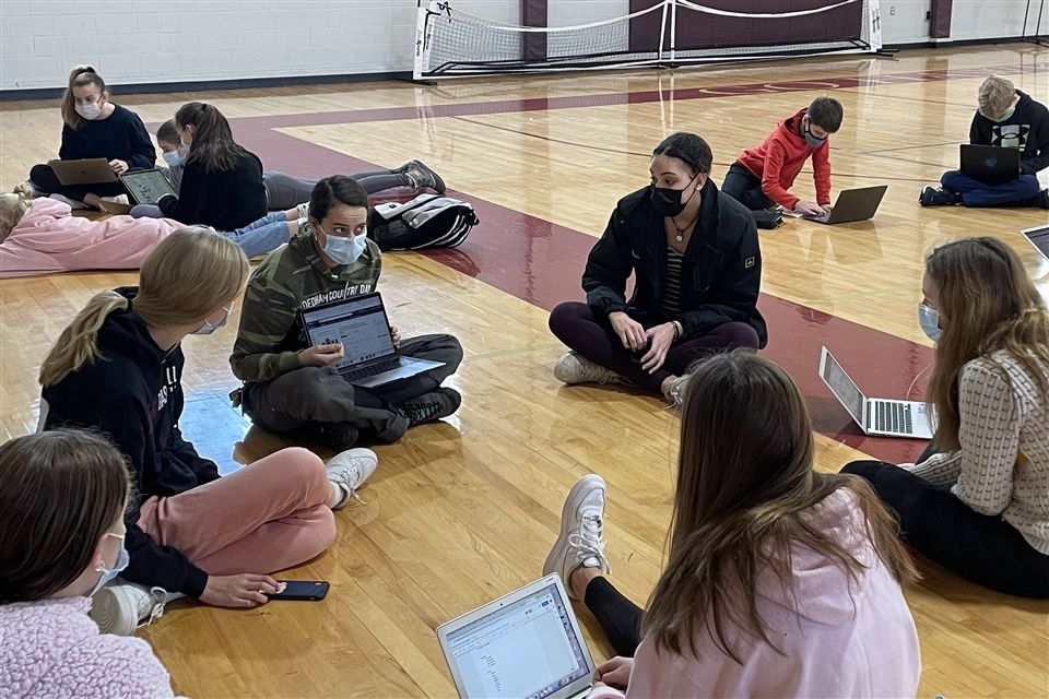 Children sitting on gymnasium floor with laptop computers