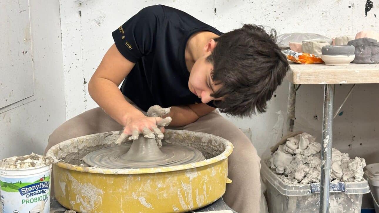 Boy sitting at potters wheel working on a pot